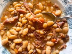 a white bowl filled with beans and ham on top of a blue and white plate