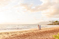 a man and woman standing on top of a sandy beach next to the ocean under a cloudy sky