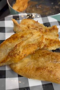 two pieces of fried chicken sitting on a checkered table cloth next to a frying pan