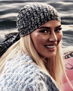 a woman is smiling while sitting on a surfboard in the water and wearing a bandana