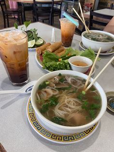 a bowl of soup with chopsticks in front of it and two drinks on the table