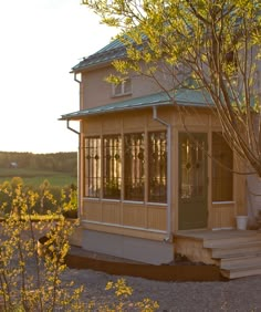 a small house sitting on top of a dirt field next to a tree and bushes