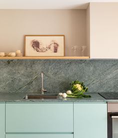 a kitchen with marble counter tops and green cabinetry in the corner, along with an art print on the wall