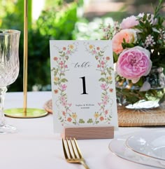 a table setting with place cards and flowers in vases on the table, along with gold cutlery