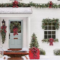 a white house decorated for christmas with wreaths and bows on the front door,