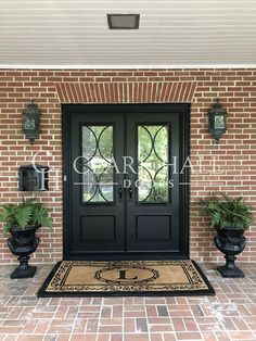 a black double door with two planters on either side and a welcome mat in front