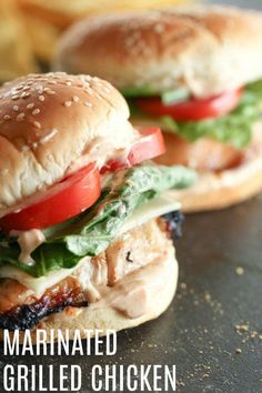 two grilled chicken sandwiches with tomatoes, lettuce and tomato on them sitting on a table