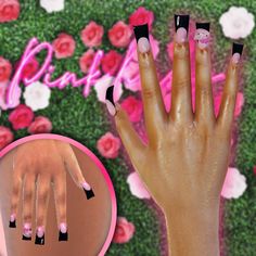 a woman's hand with black and pink nail polish on it next to flowers