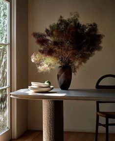 a vase sitting on top of a table next to a bowl and plate near a window