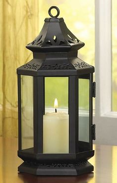 a lit candle sitting on top of a wooden table next to a window with yellow curtains