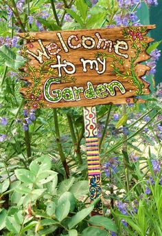 a wooden sign that says welcome to my garden in front of some flowers and plants