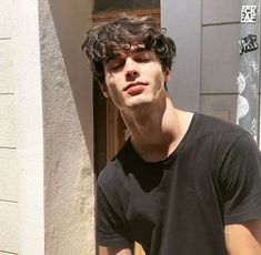 a young man standing in front of a building holding a cell phone to his ear