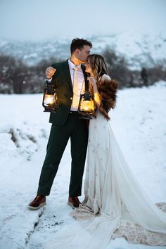 a bride and groom standing in the snow holding lanterns with their faces close to each other