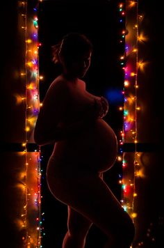 a pregnant woman standing in front of christmas lights