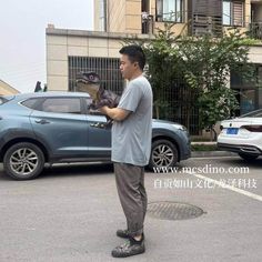 a man standing in the middle of a parking lot holding a small animal up to his face