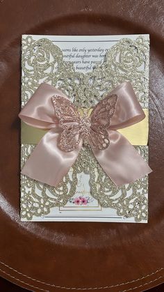 a card with a pink bow on it sitting on top of a brown plate in front of a wooden table