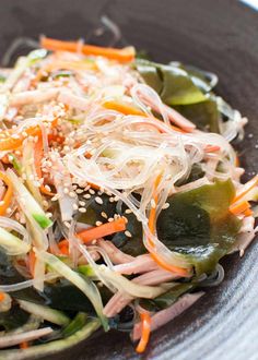 a salad with carrots, peppers and sesame seeds in a black bowl on a table