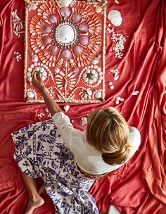 a woman laying on top of a bed next to a red cloth covered wall hanging