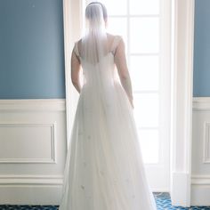 a woman in a wedding dress looking out the window with her veil draped over her head