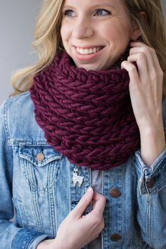 a smiling woman wearing a knitted cowl in front of a denim jacket and jean jacket