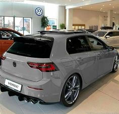 the rear end of a grey car in a showroom with other cars on display