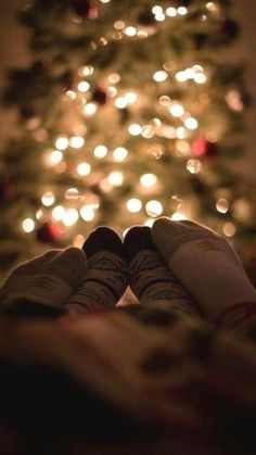 someone is holding their feet up in front of a christmas tree with lights on it