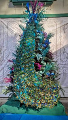 a very colorful christmas tree sitting in front of a white wall and blue tarp