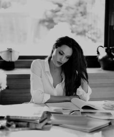 a woman sitting at a table with an open book in front of her and looking down