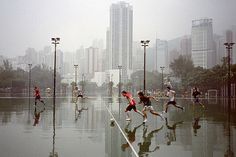 a group of people running in the rain on a city street with tall buildings behind them