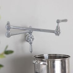 a metal pot is sitting next to a wall mounted faucet with two handles