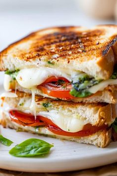 a grilled cheese and tomato sandwich on a white plate with basil leaves next to it