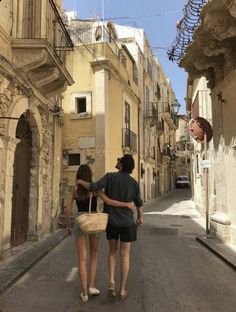 a man and woman walking down the street in front of buildings with balconies