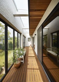 a long wooden deck with potted plants on the side and large glass doors leading to another room