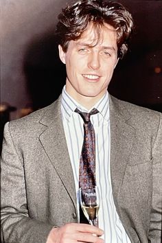 a man wearing a suit and tie holding a glass of wine in his right hand