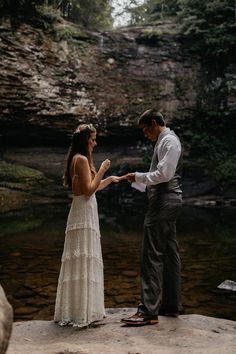 a man and woman standing on top of a rock next to a river