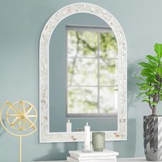 a mirror sitting on top of a table next to a vase with a plant in it