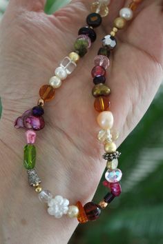 a woman's hand holding a multicolored beaded bracelet with flowers and pearls