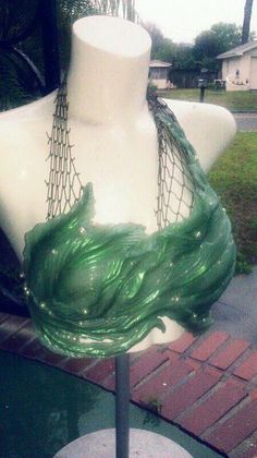 a white mannequin with green hair sitting on top of a glass table next to a brick sidewalk