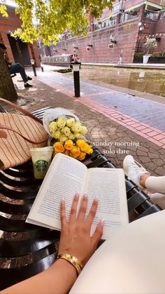 a woman sitting on a bench reading a book and holding her hand up to the open book