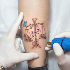 a tattoo artist working on a woman's leg with the scale of justice and flowers