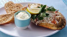 a white plate topped with food and a cup filled with cream cheese next to bread