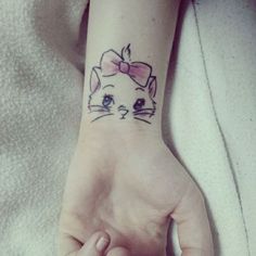 a woman's hand with a cat tattoo on her left wrist, and a pink bow around the wrist