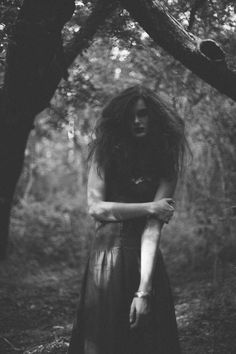 a woman standing in the woods with her hands on her chest and arms around her neck