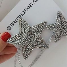 a person holding up a silver star brooch on a white card with the words broshokway written across it