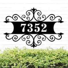 a black metal address sign mounted to the side of a white brick wall next to bushes