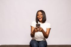 a woman sitting on a couch looking at her cell phone while laughing and holding it