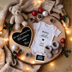 a baby's first christmas outfit, booties and teddy bear on a wooden tray