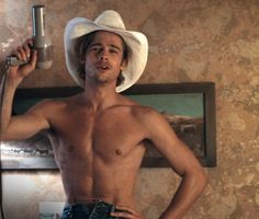 a shirtless man wearing a cowboy hat and holding an object in his right hand