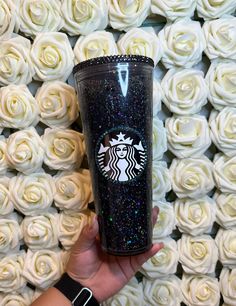 the starbucks cup has glitter on it and is in front of white roses with black sparkles