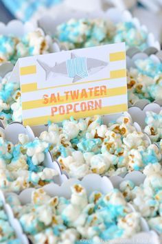 a box filled with popcorn covered in blue and yellow sprinkles next to a sign that says saltwater popcorn